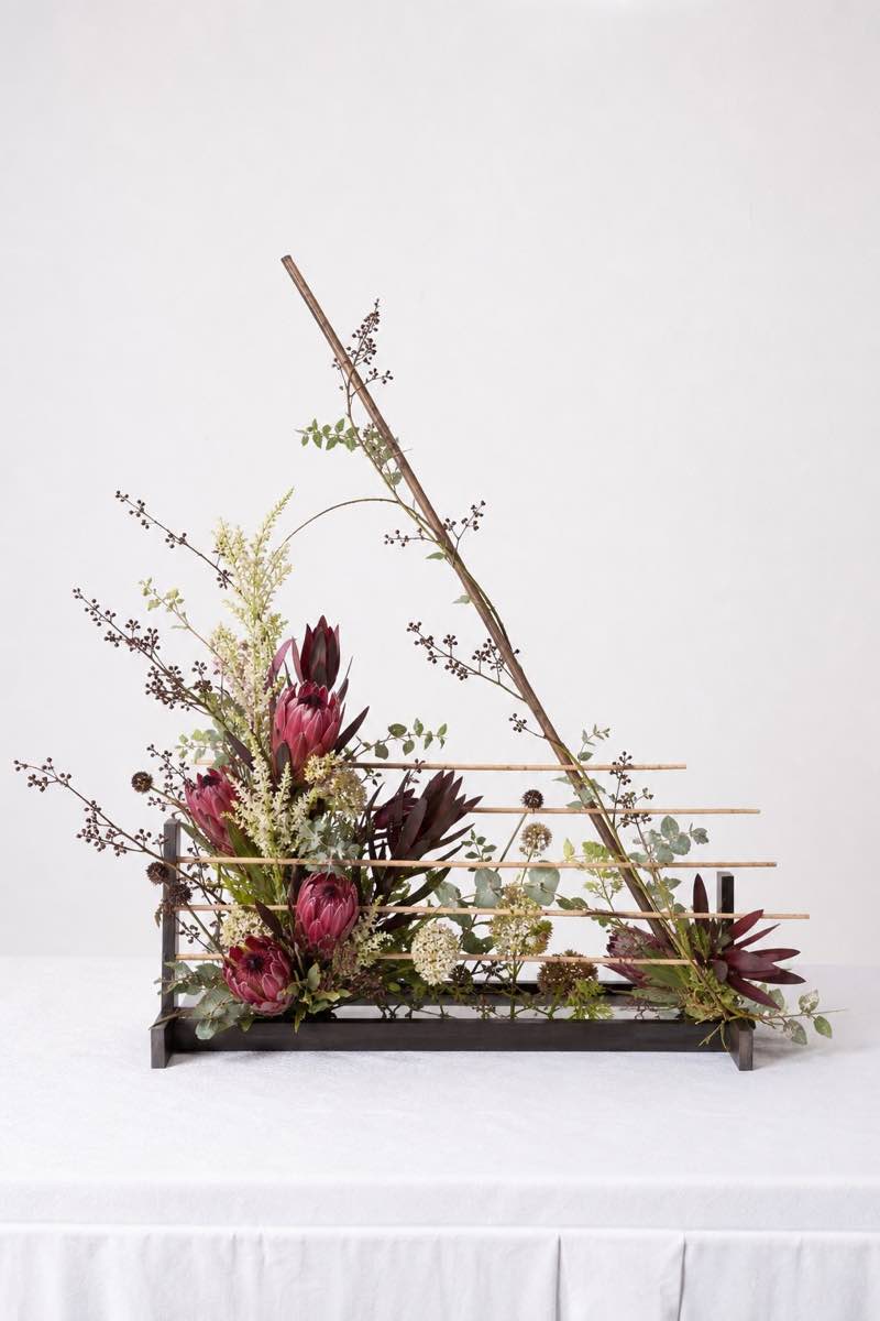 Voorbeeld in portretformaat van ’n kontemporêre Tussen lyne-rangskikking met ’n raam, proteas en sigbare horisontale en diagonale lyne.